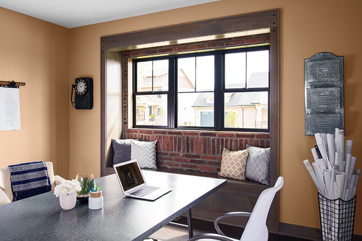 Modern home office with desk, laptop, and window seating in warm-toned room