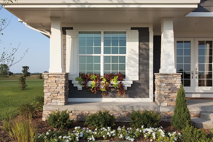 Modern residential home porch with white columns, stone pillars, and landscaped flower beds