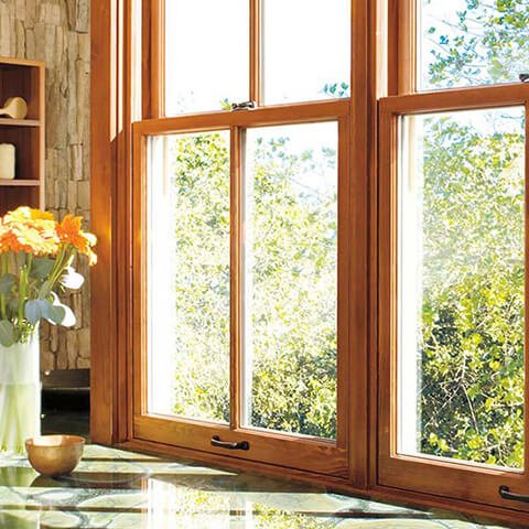 Bright kitchen with large wooden windows overlooking green trees and orange flower vase on counter