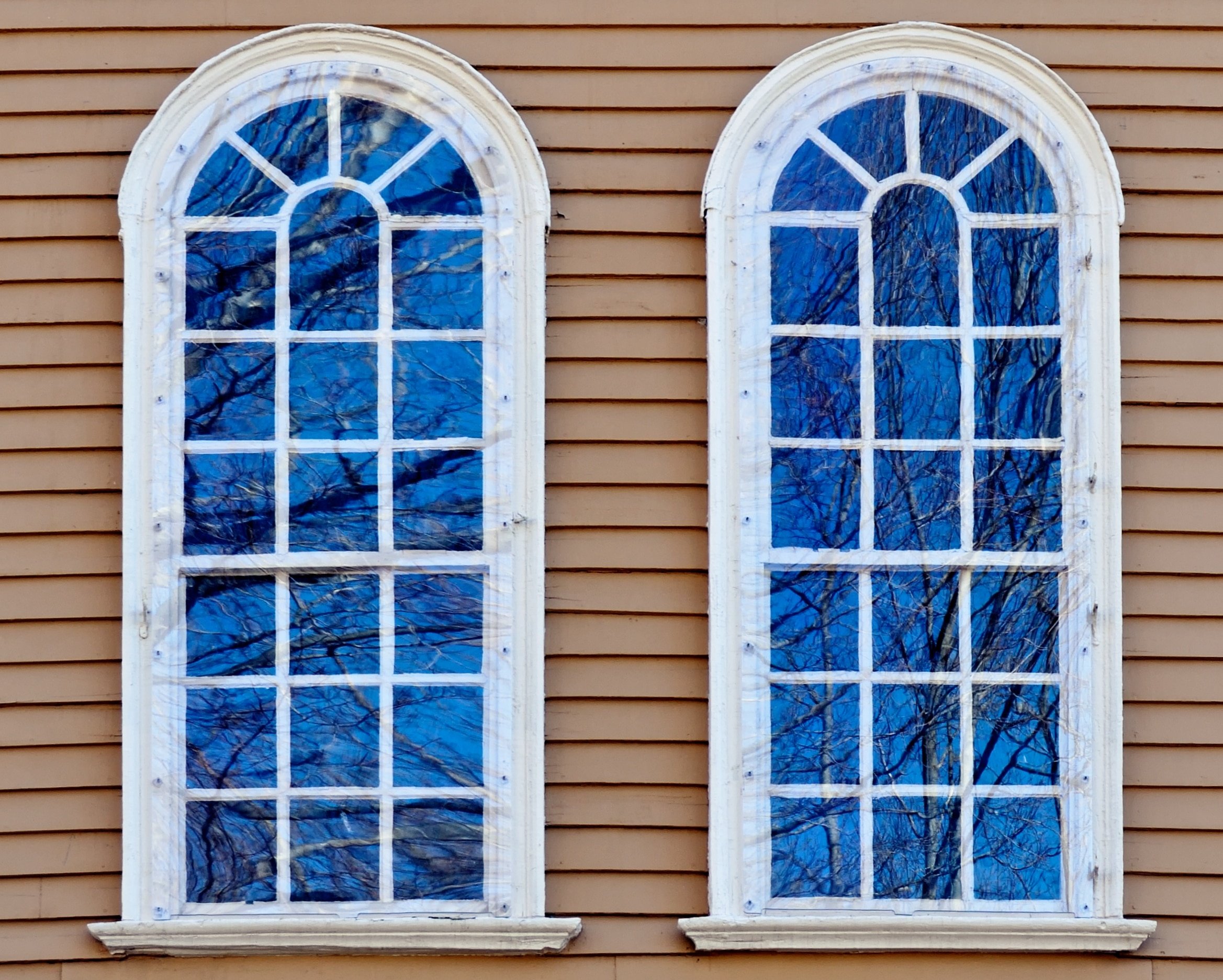 Two symmetrical arched windows with white frames on a tan siding exterior wall