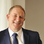 Professional business headshot of a smiling man in navy blazer and tie
