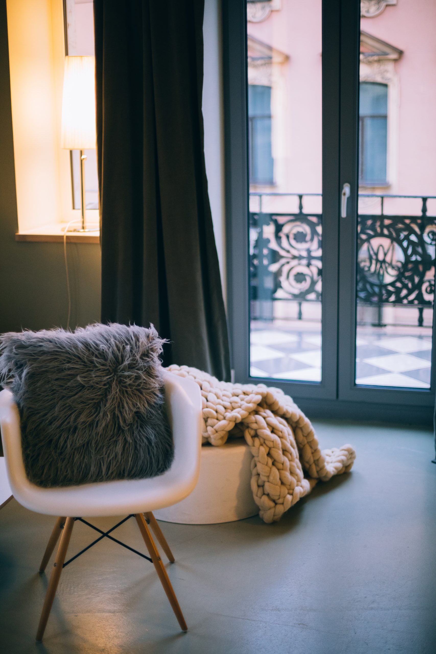 Modern white chair with black pillow and knit blanket by Parisian windows
