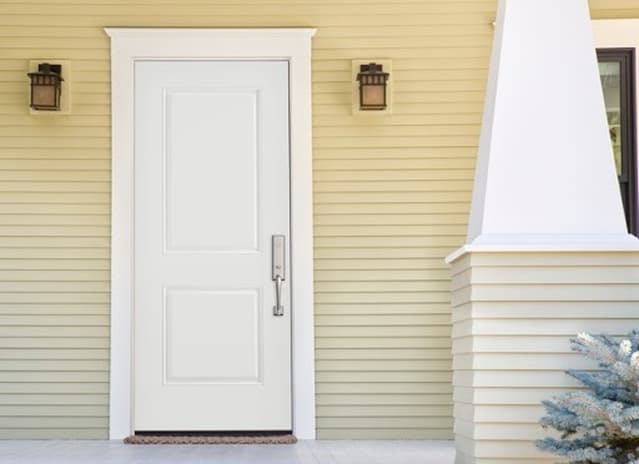 Modern white entry door on yellow siding exterior with white trim and bronze lighting fixtures
