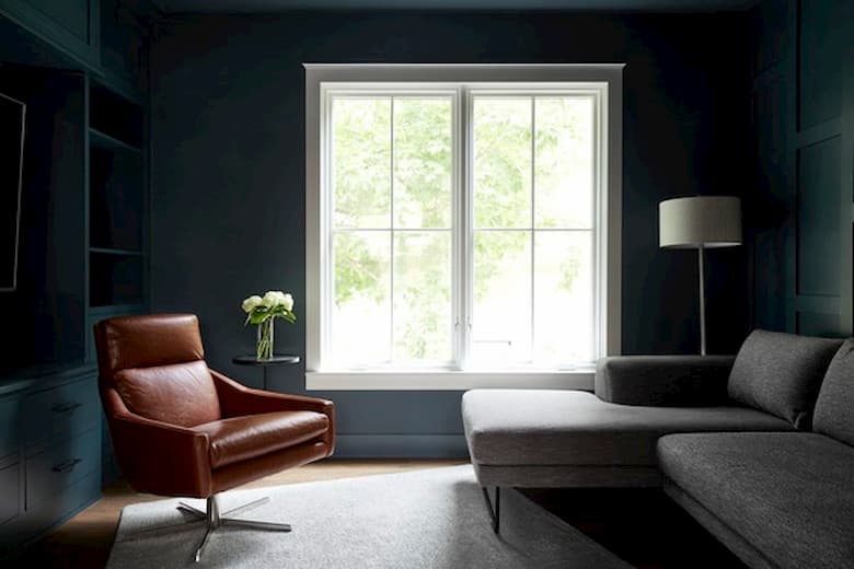 Modern living room with dark teal walls, leather chair, gray sofa, and natural light from large windows