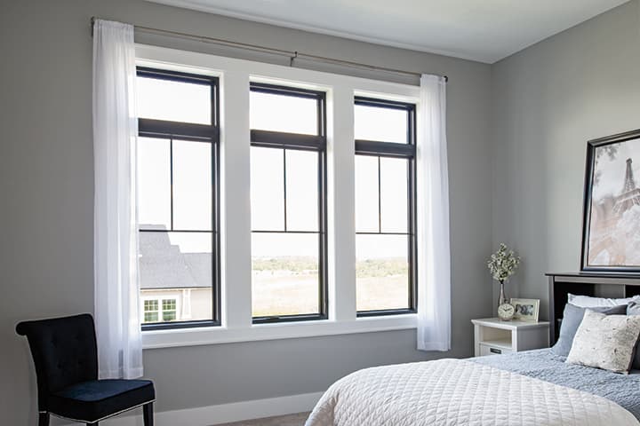 Modern bedroom with large black-framed windows, white curtains, and contemporary furniture with landscape view