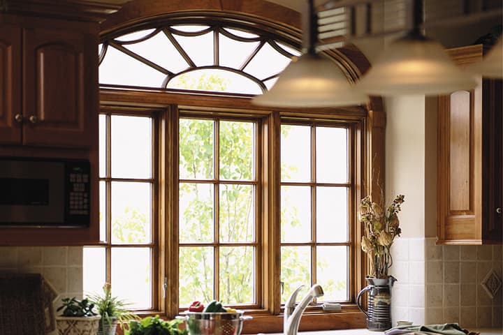 Bright kitchen with large wooden windows, sink, plants, and natural daylight streaming through fanlight