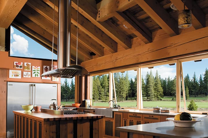 Modern kitchen with wood beams and expansive windows overlooking forest landscape