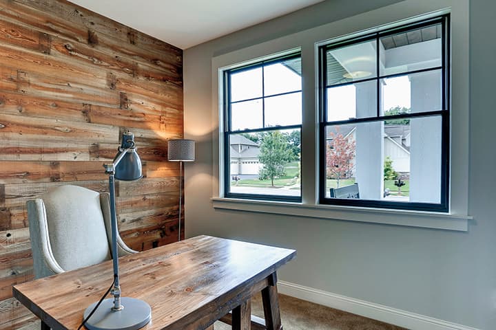 Modern home office with wooden desk, task lamp, and large windows overlooking neighborhood
