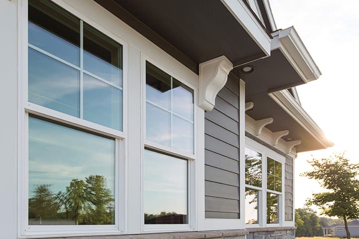 Modern home with large white-framed windows reflecting blue sky and trees