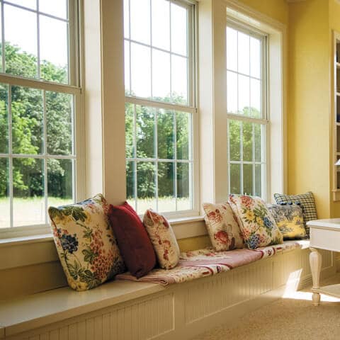 Bright window seat with decorative pillows overlooking a green garden in a cheerful yellow room