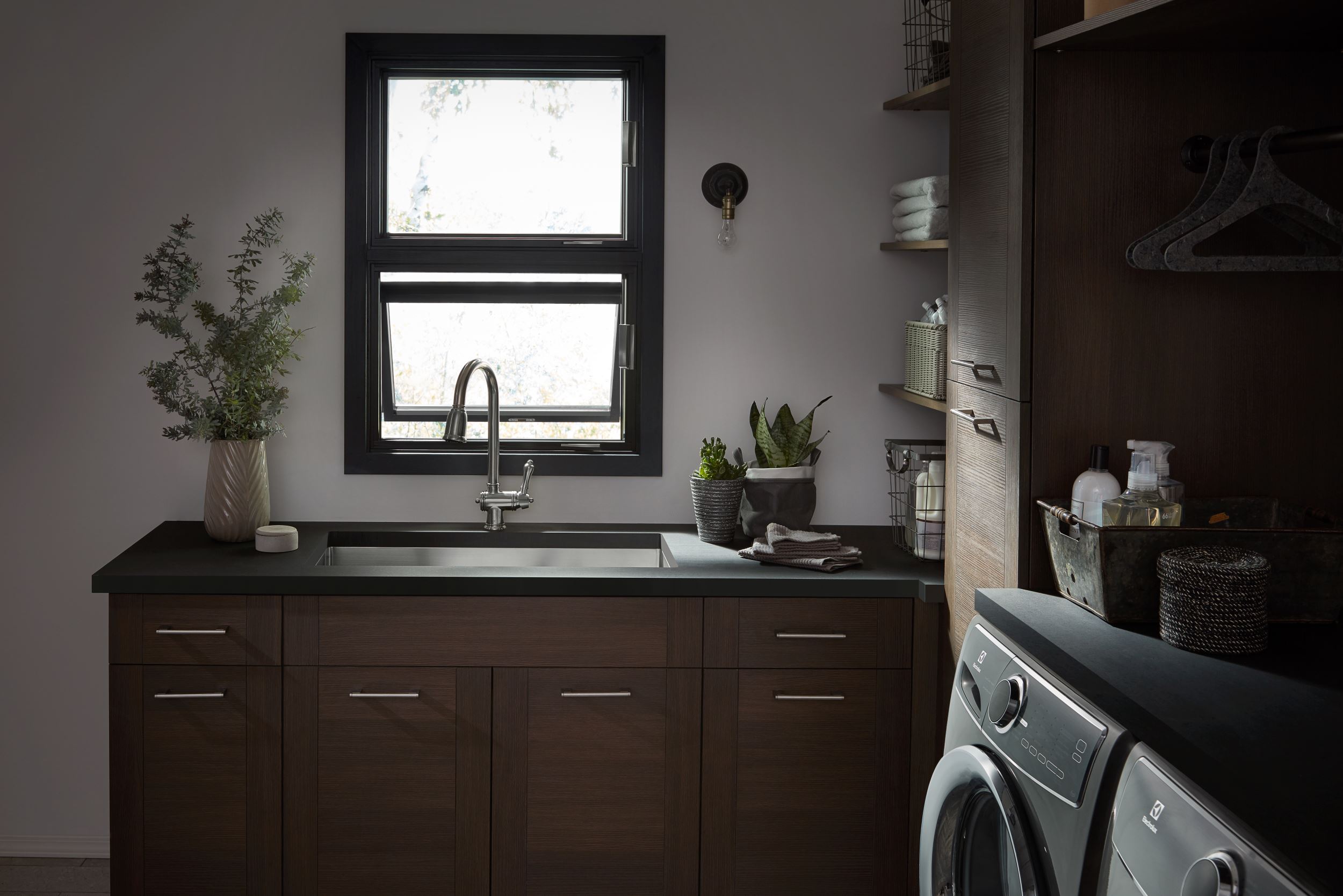 Modern laundry room with dark cabinetry, stainless steel sink, and stacked washer dryer units