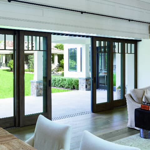 Modern interior with black-framed sliding glass doors opening to lush green garden and patio