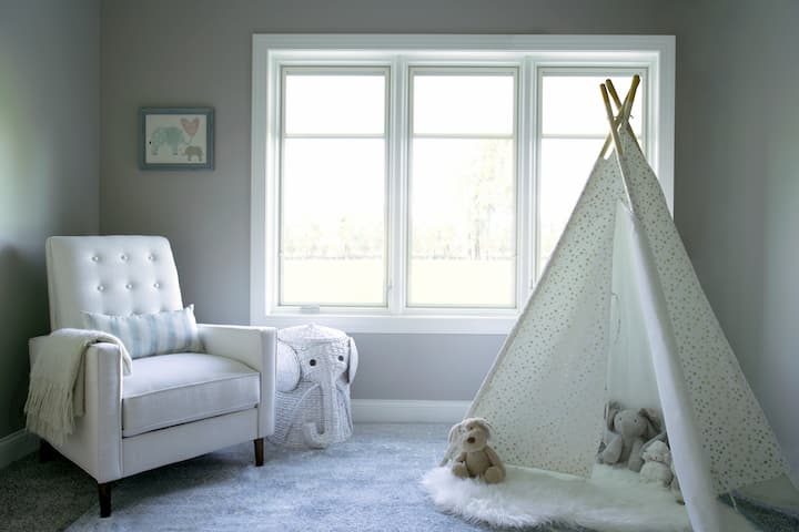 Modern nursery with glider chair and gray patterned teepee tent by windows