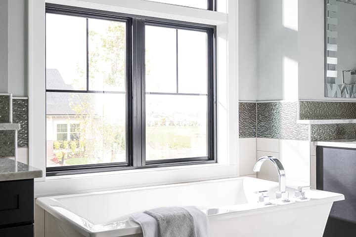 Modern luxury bathroom with white bathtub and black-framed windows overlooking nature
