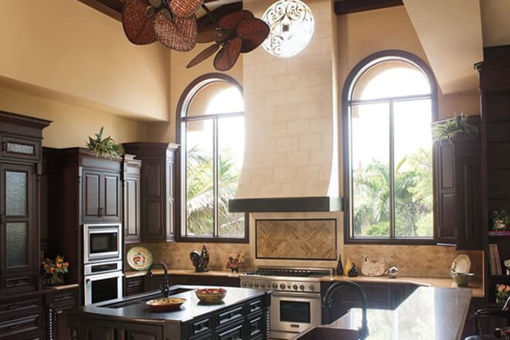 Luxury kitchen with dark cabinetry, granite counters, and arched windows overlooking tropical landscape