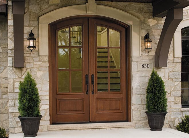 Elegant residential front entrance with double wooden doors and symmetrical topiary planters