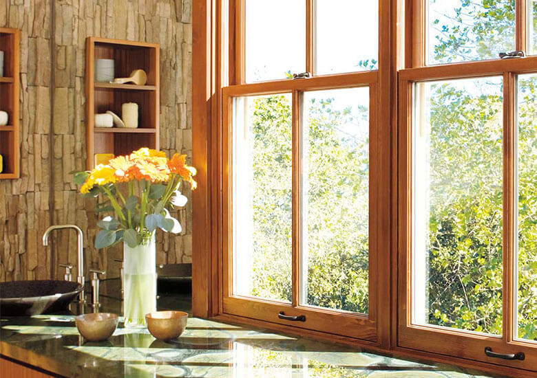 Modern kitchen with wooden windows, granite countertop, and yellow flowers overlooking green landscape