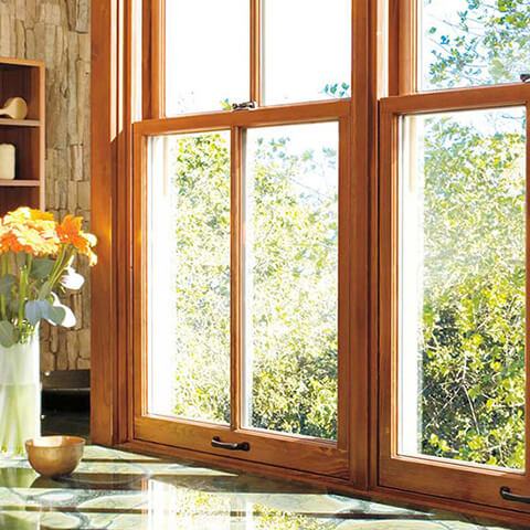Bright kitchen with large wooden windows overlooking green trees and orange flower vase on counter