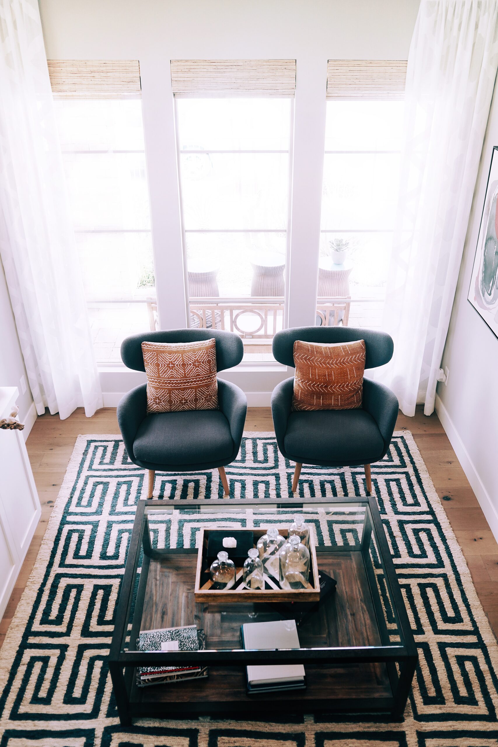 Modern living room with teal chairs, geometric rug, and floor-to-ceiling windows